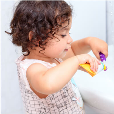 child putting toothpaste on toothbrush